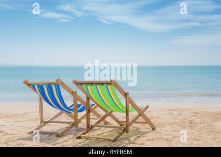 Due sedie a sdraio sulla sabbia bianca con l'azzurro del cielo e del mare di estate sfondo. Estate, vacanze, viaggi e vacanze concetto. Foto Stock