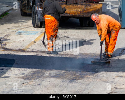 Lavoratore regolare la posa di nuovo asfalto per applicare una patch a un urto in strada. Foto Stock