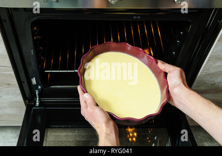 Preparazione cuocere la torta. Dell'uomo mette le mani di forma con la pastella in forno. Foto Stock