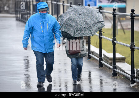 La gente a prendere un wet passeggiando lungo la promenade a Porthcawl Galles, dove i venti forti e pioggia è caduta nella zona come un avviso di colore giallo per il vento è ancora in posizione attraverso parti del Regno Unito. Foto Stock