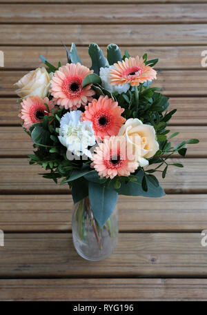 Un bouquet fatto di coloratissimi fiori misti. Non c'è rosa, arancione, giallo e bianco fiori in un vetro trasparente vaso. Il vaso è su un pavimento di legno. Foto Stock