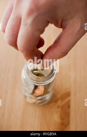 La mano di mettere una moneta in un barattolo di risparmio Foto Stock