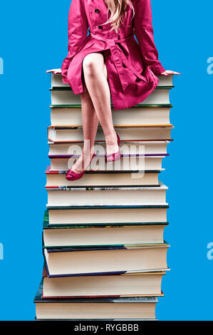 donna in cappotto rosso seduta su una pila di libri - giornata del libro del mondo Foto Stock
