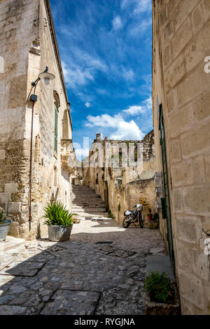 Giorno di estate scenario street view del sorprendente antica città dei Sassi con moto e puffy bianche nuvole che si muovono italiana sul cielo blu. Matera, Basilicata, Italia Foto Stock