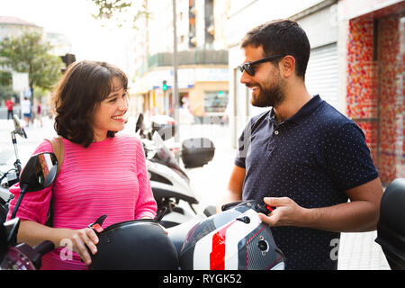 Felice e attraente coppia giovane mettendo su i loro caschi a guidare la moto per la città Foto Stock