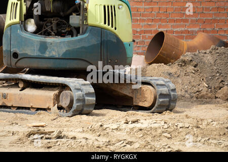 Piccolo caricatore cingolato scava nel parco trincea per la posa di tubazioni Foto Stock