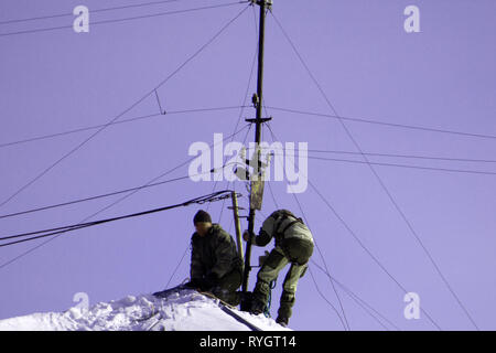 Team di lavoratori di sesso maschile pulire il tetto dell'edificio da neve con pale in cinghie di fissaggio del mantra Foto Stock