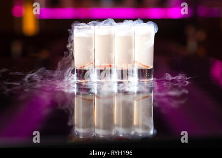 Quattro cocktail bianco scatti con fumo su specchio riflettente tabella con luci al neon color porpora Foto Stock