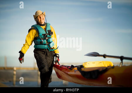 Sorridente donna senior portando la fine di un kayak al sole. Foto Stock