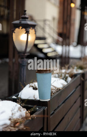 Mockup annuncio: una carta vergine cup in piedi su una recinzione in una vecchia città sullo sfondo Foto Stock