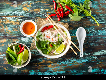 Tradizionale zuppa vietnamita Pho bo con erbe aromatiche, di carne o di riso tagliatelle, brodo. Pho bo nella ciotola con bacchette, cucchiaio. Vista dall'alto. Asian soup Pho bo, legno t Foto Stock