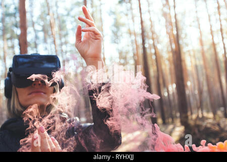 Una donna che indossa la realtà virtuale occhiali nella foresta vede fumo bombe. Occhiali VR. Foto Stock