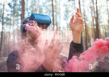 Una donna che indossa la realtà virtuale occhiali nella foresta vede fumo bombe. Occhiali VR. Foto Stock