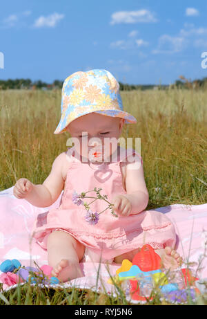 Carino bambina in un cappello seduti sulla coperta rosa, verde e azzurro del cielo in background Foto Stock