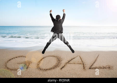 Jumping imprenditore il tifo per obiettivo la parola scritta sulla spiaggia di sabbia di sfondo Foto Stock