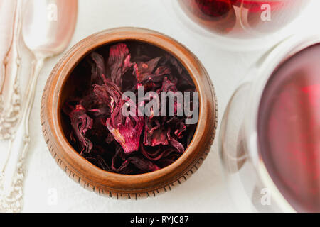 Asciugare i fiori di ibisco rosso tè in una ciotola di legno vicino su sfondo bianco, vista da sopra Foto Stock