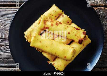 Close-up di crepes panini con formaggio cremoso ripieno su una piastra di nero su un vecchio tavolo di legno. vista da sopra, flatlay Foto Stock