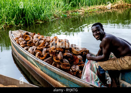 L'uomo il riempimento di un sacchetto con gusci di noce di cocco in una canoa in Grand Bassam, Costa d'Avorio. Foto Stock