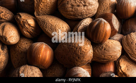 Close-up di un mucchio di noci, nocciole e mandorle marrone, frutta secca con luce morbida Foto Stock