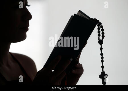 Silhouette di una donna cristiana della lettura della Bibbia con grani di preghiera. Il Vietnam. Foto Stock