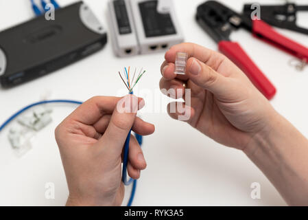 Il tecnico tenendo un doppino internet via cavo e connettore maschio RJ45. Il tecnico di riparazione rete con pinza a crimpare per cavo Foto Stock