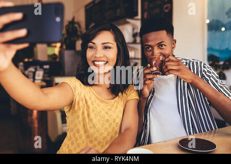 Giovane donna prendendo selfie con il suo amico di bere il caffè in un bar. Giovani amici seduti insieme al coffee shop tenendo selfie. Foto Stock