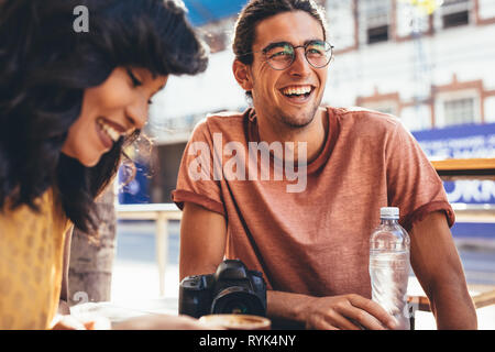 Sorridente giovane uomo che parla con gli amici presso il cafe. Le persone creative che incontro al city cafe. Foto Stock