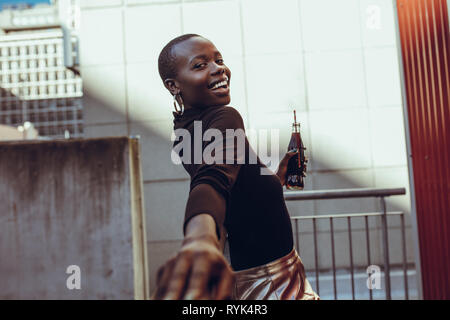 Felice giovane donna africana appoggiata ad una ringhiera con soft drink. Donna allegra godendo una giornata fuori. Foto Stock