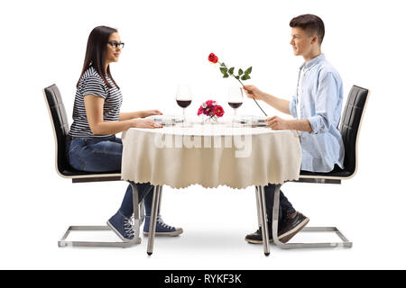 A piena lunghezza profilo di un giovane maschio dando una rosa di una giovane donna in un ristorante tabella isolati su sfondo bianco Foto Stock