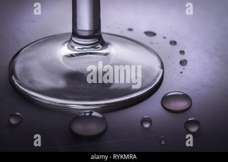 Close-up di un elegante bicchiere di vetro con la bevanda alcolica e di gocce di acqua su metallico e la superficie riflettente Foto Stock