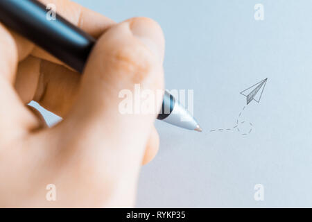 Close-up di un essere umano del disegno a mano su un foglio bianco con un nero elegante penna a sfera e il disegno di un aeroplano di carta come per inviare un messaggio Foto Stock