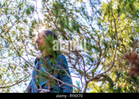 Vista laterale della giovane donna che indossa abiti casual camminando tra la vegetazione in un luminoso giorno Foto Stock