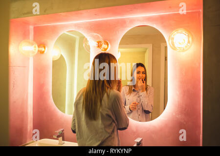 La donna dipinge le labbra nel WC. Attraente donna felice di applicare il trucco nel bagno di un ristorante - Immagine Foto Stock