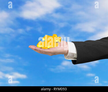 La mano che mostra l'oro puzzle pezzo con blue sky nuvole sullo sfondo Foto Stock
