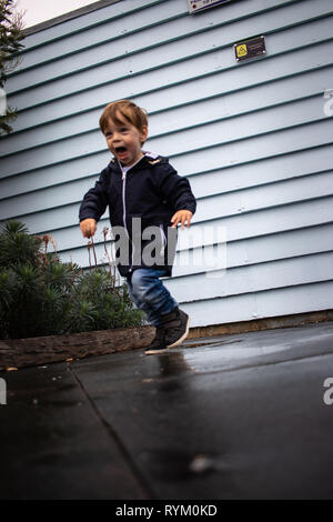 Piccolo Ragazzo in esecuzione attraverso pozzanghere e sorridente Foto Stock