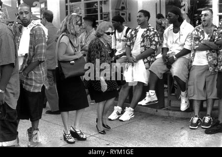 South Beach Ocean Drive Miami Florida 1990 Stati Uniti. Due donne d'affari che osservano stressate spingono attraverso una folla di giovani uomini afroamericani appesi fuori durante la pausa estiva. 1999 HOMER SYKES Foto Stock