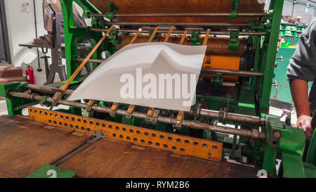 Il grande vecchio manuale macchina di stampa all'interno della fabbrica essendo azionato dal lavoratore all'interno Foto Stock