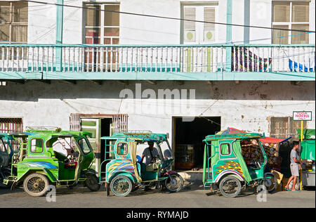 Romblon, Romblon Provincia, Filippine: Tre tricicli verde nel centro della città di attesa per i passeggeri, vecchi edifici in background Foto Stock