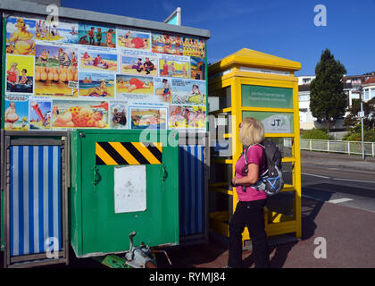 Donna escursionista guardando Cheeky cartoline su Tea Van accanto a un giallo casella Telefono vicino a St Helier sull'isola di Jersey, nelle Isole del Canale, UK. Foto Stock