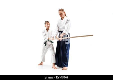 Uomo e teen boy combattimenti con la spada in legno a Aikido la formazione nella scuola di arti marziali. Uno stile di vita sano e sport concetto. Fightrers in kimono bianco su sfondo bianco. Il Karate di uomini in uniforme. Foto Stock