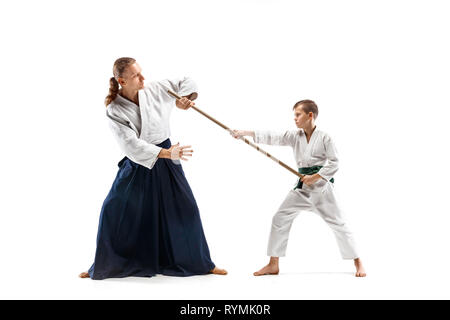 Uomo e teen boy combattimenti con la spada in legno a Aikido la formazione nella scuola di arti marziali. Uno stile di vita sano e sport concetto. Fightrers in kimono bianco su sfondo bianco. Il Karate di uomini in uniforme. Foto Stock