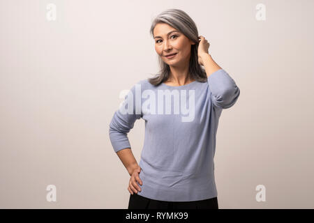 Sorridente donna asiatica tocca i suoi capelli grigi Foto Stock