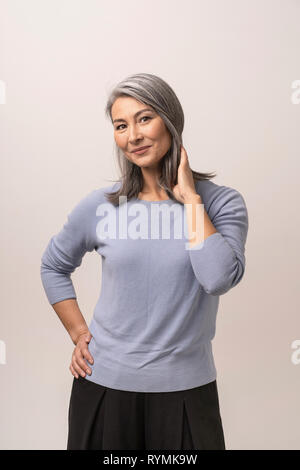 Sorridente donna asiatica tocca i suoi capelli grigi Foto Stock