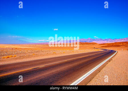 Deserto autostrada che conduce attraverso il deserto arido verso montagne brulle al di là. Foto Stock