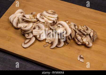 Funghi su un bordo di taglio durante la fase di pulizia e taglio come parte del processo di preparazione di champignon freschi per congelamento successivo Foto Stock