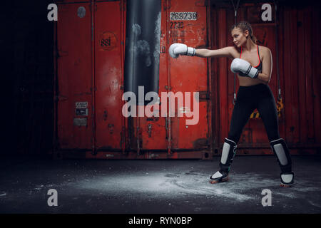 Boxer femmina di colpire un enorme sacco da boxe presso un studio di inscatolamento. Donna boxer allenamento duro. Foto Stock