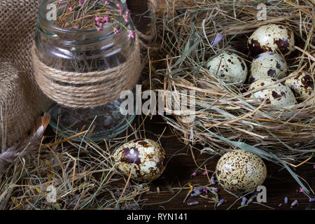 La pasqua ancora in vita. Uova di quaglia nel nido e sul vecchio tavolo in legno nel granaio tra il fieno e fiori secchi. Foto Stock
