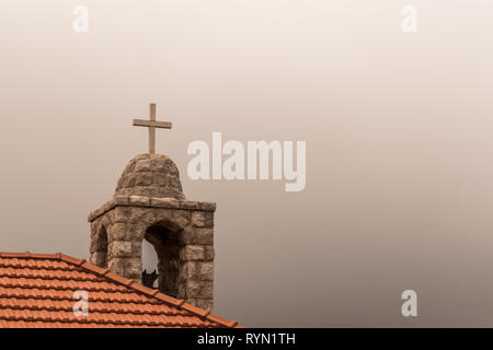 Questa cattura mostrano la croce di una chiesa prese con cielo coperto con la nebbia e la nebbia e si può vedere dentro la cupola sit una campana Foto Stock