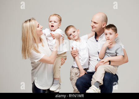 Grande e allegra famiglia mamma, papà e tre figli. Felice insieme. ritratto di famiglia su sfondo grigio chiaro. Foto Stock