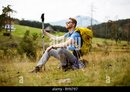 Bel giovane capelli rossi backpacking uomo resto presso la collina Foto Stock